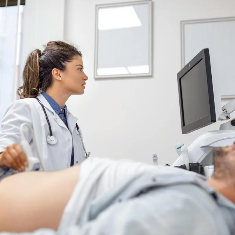 Medical professional conducting an abdominal ultrasound on a patient, with the ultrasound monitor visible in the background